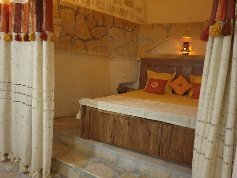 Chambre de Dar Zmen : mur de pierre, lit en bois et rideaux tissés